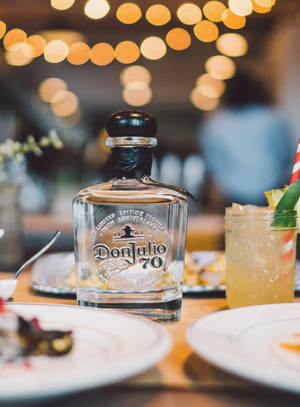 一瓶Don Julio 70龍舌蘭酒，配以雞尾酒和甜點，放在木桌上，在溫暖的燈光下。