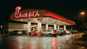 夜晚的Chick-fil-A餐廳，帶有發光的紅色霓虹燈標誌和潮濕停車場的倒影。