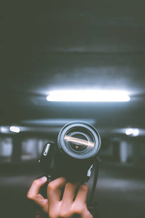 在螢光燈照亮的黑暗停車場中，一隻手拿著黑色Canon相機。