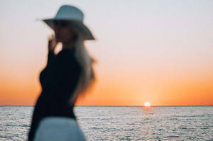 戴帽子的女人剪影，以海洋日落為背景