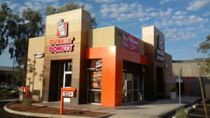 在藍天下，帶有橙色點綴和得來速標誌的Dunkin' Donuts餐廳。 — 冬甩 壁紙