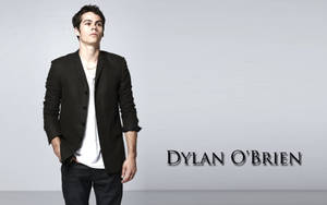 演員 Dylan O'Brien 身穿黑色西裝外套和白色T恤在工作室中擺姿勢。