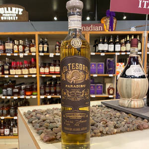一瓶 El Tesoro Paradiso 龍舌蘭酒放在酒類商店的鵝卵石展示架上。