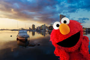 Elmo 在日落時分的港口前微笑，背景有船隻和城市天際線。 — MacBook Pro 壁紙