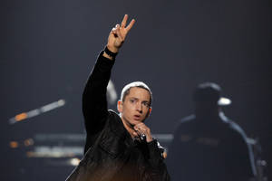 Eminem 在舞台上手持麥克風和平手勢表演。
