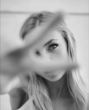 一位金髮女性在黑白肖像中透過模糊前景元素凝視。