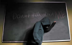 一個穿連帽衫的人正在黑板上寫「Do not talk about ME」。
