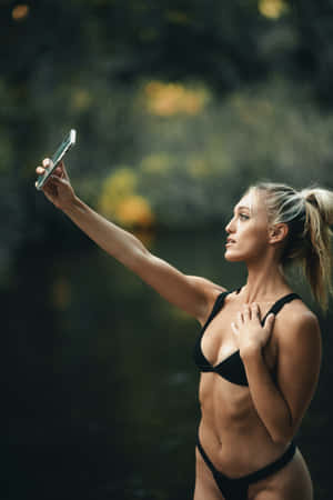 身穿黑色比堅尼嘅女士喺有霧氣同金色樹葉嘅森林溪流附近自拍。 — 比堅尼 GIF 壁紙