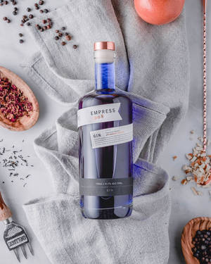 一個藍色氈酒瓶被乾燥香草和柑橘類水果包圍，放在灰色布上。