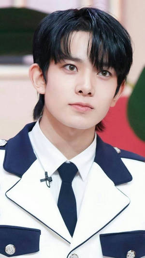 年輕男子穿著正式白色和海軍藍色制服，打黑色領帶，直視鏡頭。