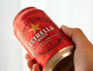 手拿著一個有冷凝水的冰凍紅色Estrella Damm啤酒罐。