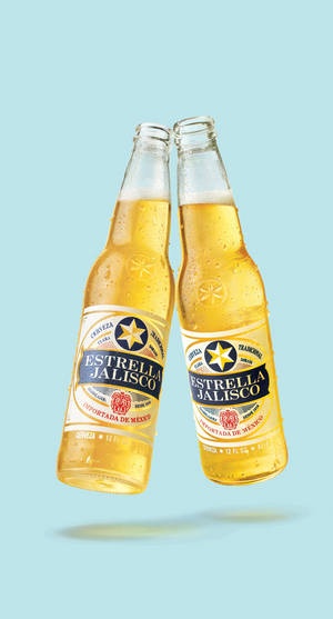 兩瓶Estrella Jalisco啤酒在藍色背景上碰撞，帶有冷凝水滴。