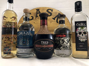 五瓶手工龍舌蘭酒和梅斯卡爾酒，帶有彩色標籤，展示在木製標誌前。