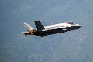 F-35戰鬥機在森林覆蓋的山脈上空飛行，後燃器啟動。