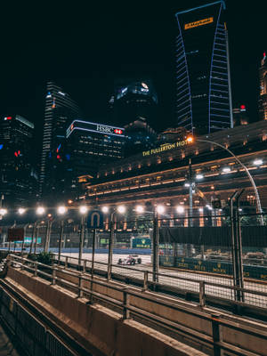 賽車在夜晚的城市賽道上飛馳，背後是燈火通明的摩天大樓。