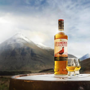 威士忌瓶和玻璃杯放在桶上，背景有雪山。