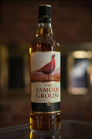 在昏暗環境中，反射表面上的 Famous Grouse 威士忌酒瓶。