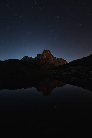 山峰和星空倒映在夜晚平靜的湖面上。