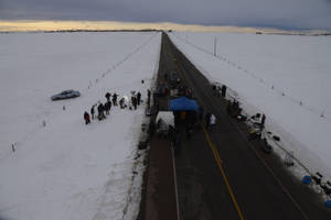 黃昏時分，冰凍田野的雪路上聚集的人群和車輛。