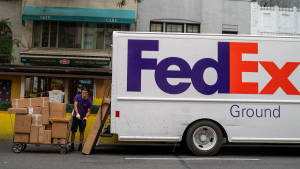 FedEx 送貨司機在城市街道上將裝有包裹的手推車推到送貨卡車旁邊。