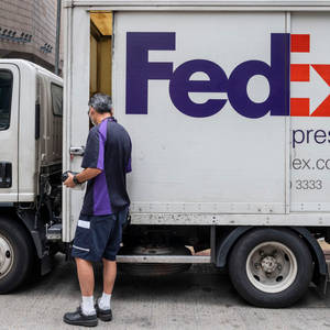FedEx送貨司機正在城市街道上將包裹裝載到白色送貨車上。