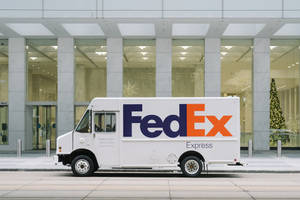 白色FedEx Express貨車停在一棟現代辦公樓前，樓內有一棵亮燈的聖誕樹。