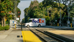 FedEx貨車停在鐵路平交道，背景有紅燈和樹木。