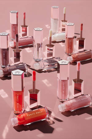 Fenty Beauty 唇彩系列以玫瑰金色包裝，置於粉紅色背景上。