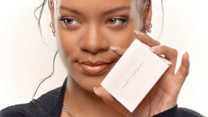 Rihanna 帶住溫柔嘅微笑，揸住一個 Fenty Beauty 化妝粉盒。