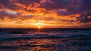 夕陽映照海洋，海浪拍打，戲劇性的橙色紫色雲彩