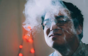 戴眼鏡的男子在室內發光燈串附近呼出煙霧。