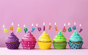 五個生日杯子蛋糕，上面有燃燒的蠟燭拼出 happy birthday。