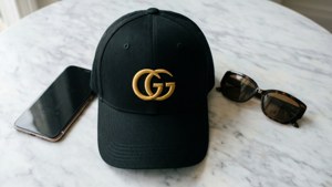黑色Gucci帽、智能手機和玳瑁太陽眼鏡放在大理石表面