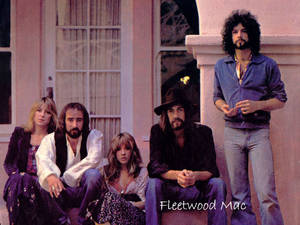 穿著70年代服裝的Fleetwood Mac樂隊成員在粉紅色建築前戶外擺姿勢。