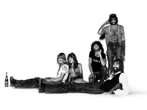 五名身穿1970年代搖滾服飾的男子在攝影棚拍攝中拿著啤酒瓶擺姿勢。