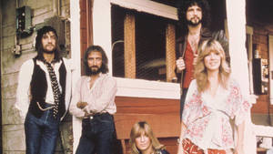 Fleetwood Mac 樂隊成員在木門廊上穿著 1970 年代風格服裝擺姿勢。