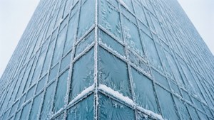 灰色天空下，一個高層玻璃建築角落覆蓋著霜和雪。