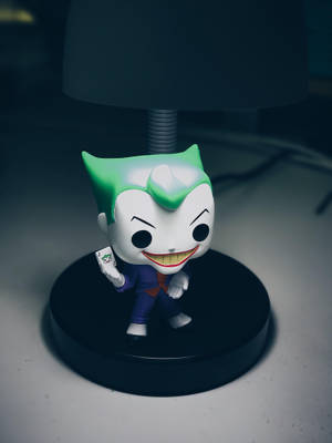 Funko Pop 小丑公仔在桌上燈下拿著小丑牌。 — 小丑 壁紙