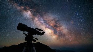 三腳架上的望遠鏡指向夜間黑暗山脈上空的銀河