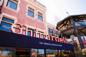 磚造建築上嘅 Ghirardelli 朱古力店招牌，背景有摩天輪同鐘樓。
