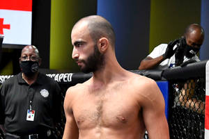 一位赤裸上身的MMA拳手在八角籠中，附近有戴口罩的工作人員。