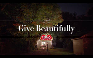 秋夜樹下木屋的夜景，帶有「Give Beautifully」和Stella Artois標誌。