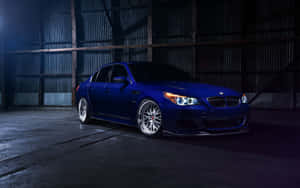 閃亮藍色BMW M5轎車配備定制輪圈，在昏暗的工業倉庫中。 — MacBook Air M1 壁紙