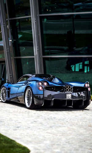 藍色Pagani Huayra停泊在玻璃建築旁的石鋪路面上。 — Galaxy Tab A 壁紙