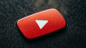 一個紅色 YouTube 播放按鈕圖示在深色紋理表面上，帶有漂浮的灰塵。