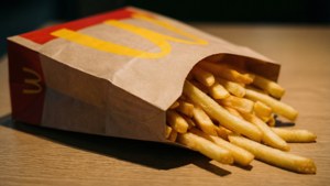 金黃色的薯條從麥當勞的袋子中灑出，落在木桌上。