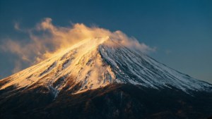 白雪覆蓋的山峰在金色的日出光芒中閃耀，雲彩在其山頂盤旋。