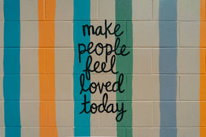 彩色條紋牆上寫有手寫訊息「make people feel loved today」