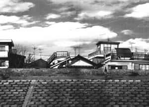 黑白城市景觀，房屋位於草地堤岸上，俯瞰磚砌運河，遠處有騎單車的人。 — 暮光 壁紙
