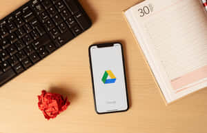 智能手機在木桌上顯示 Google Drive，配有鍵盤、計劃簿和皺紙。